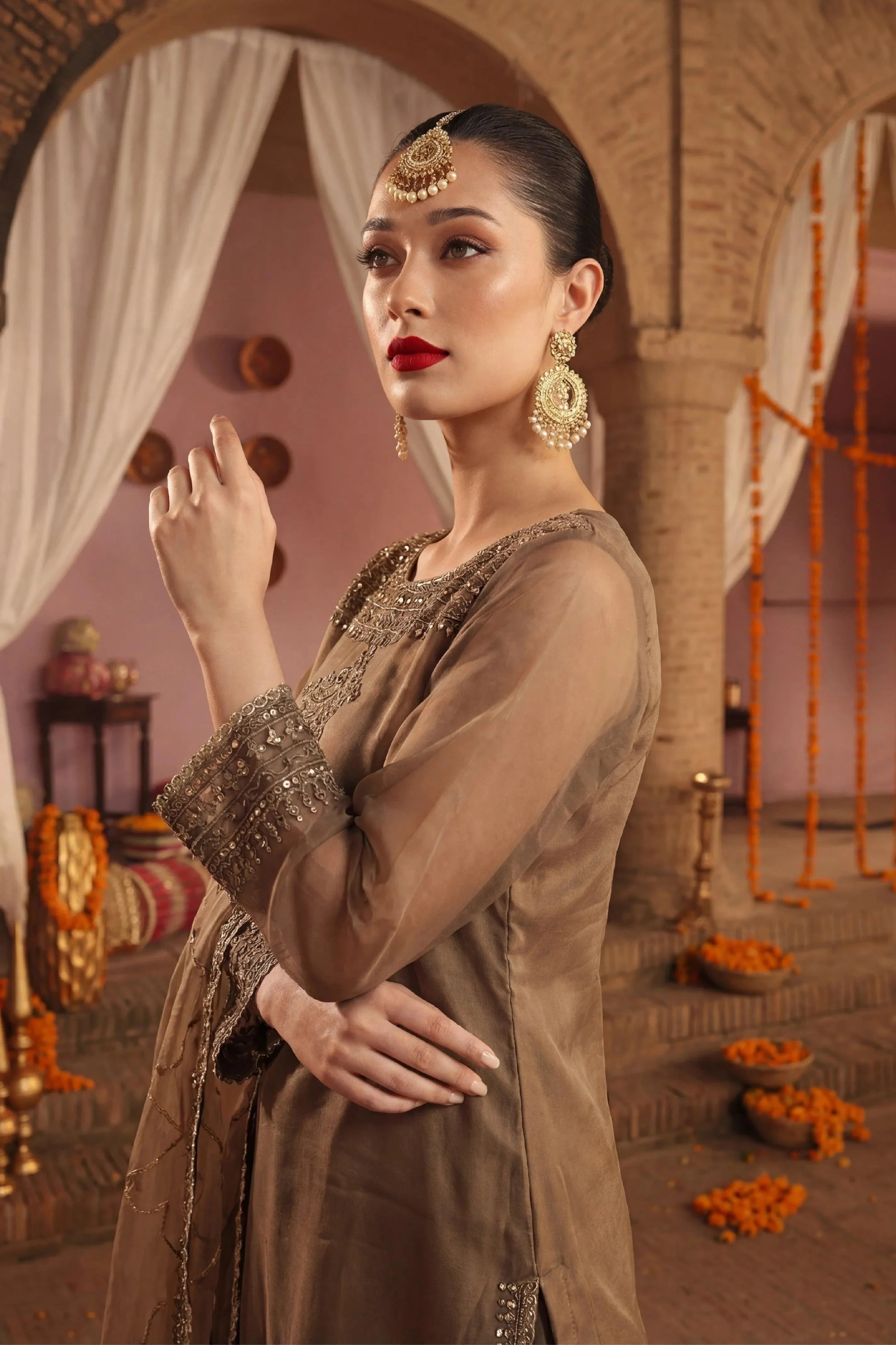 Elegant woman in embroidered brown dress with gold jewelry, perfect for Pakistani wedding or festive occasions.