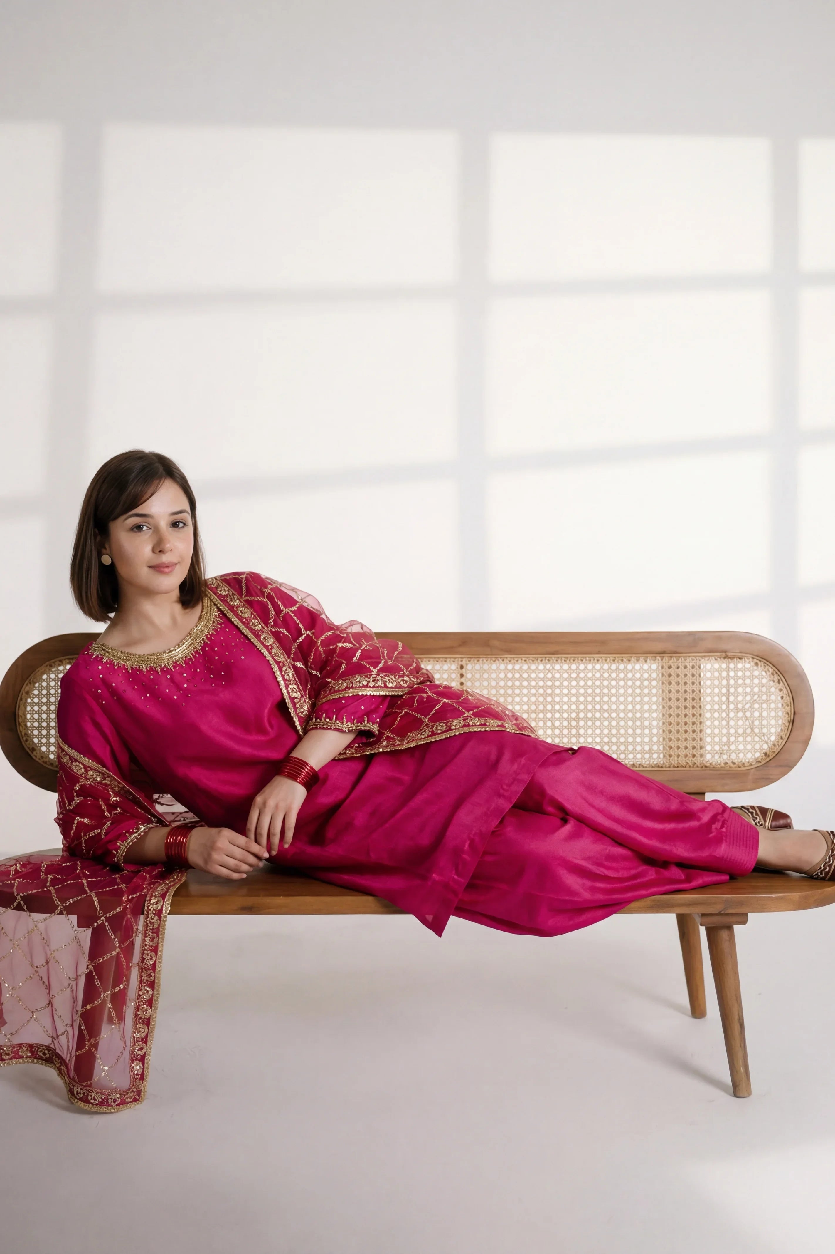 Elegant woman in pink embroidered dress, sitting on wooden bench with cane backrest