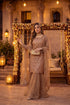 Elegant woman in shimmering gold Pakistani dress with floral arch, perfect for weddings and festive occasions.
