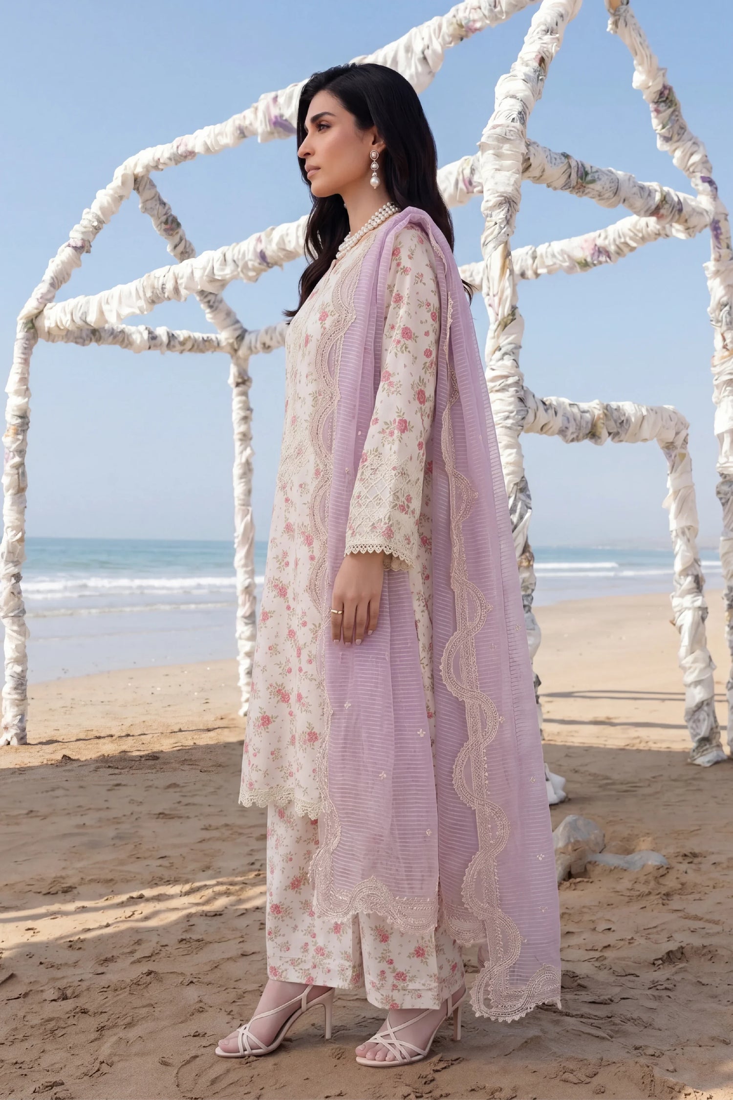 Elegant floral printed Pakistani dress with lace detailing and lavender dupatta, styled on beach