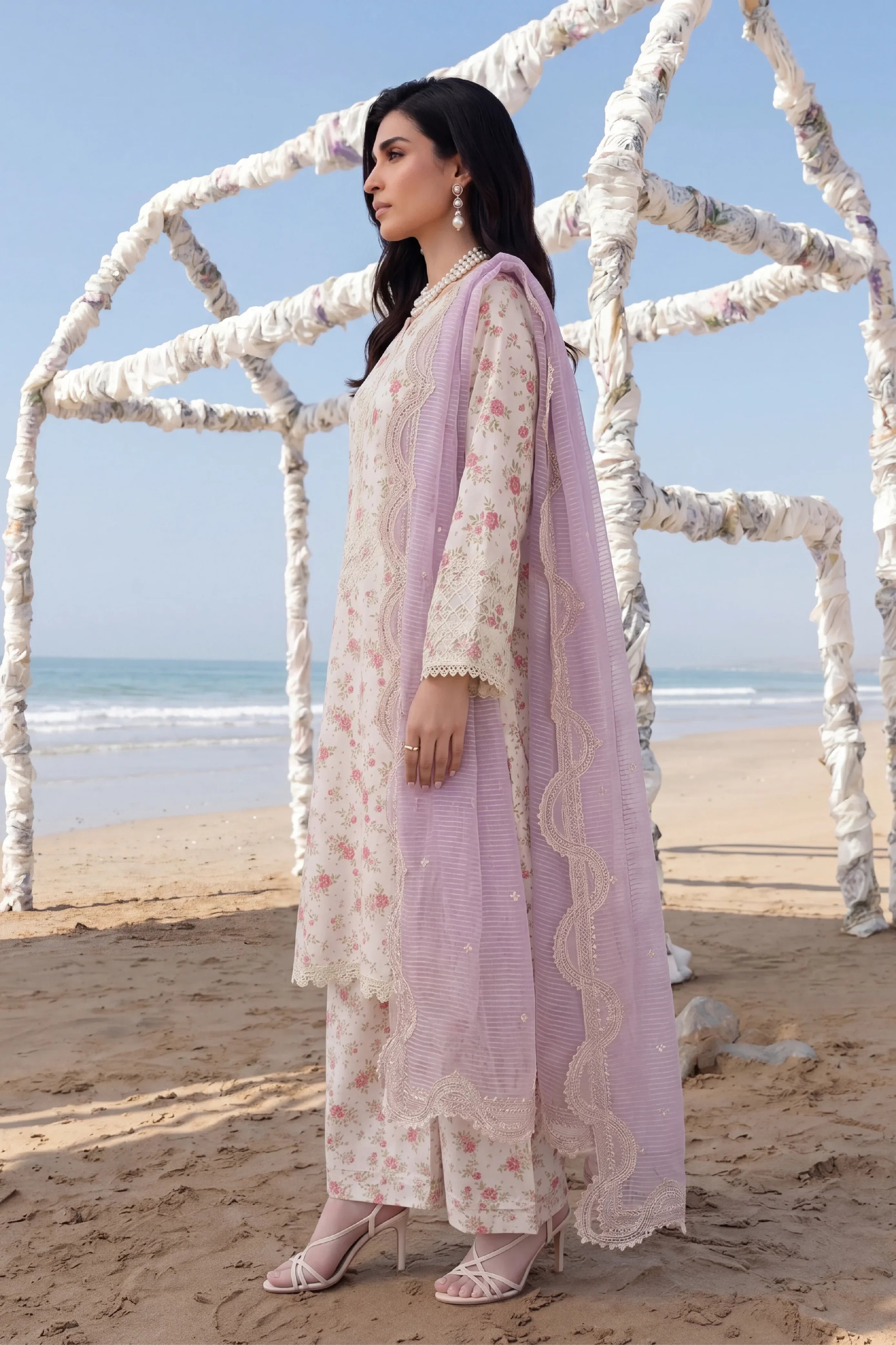 Elegant floral printed Pakistani dress with lace detailing and lavender dupatta, styled on beach