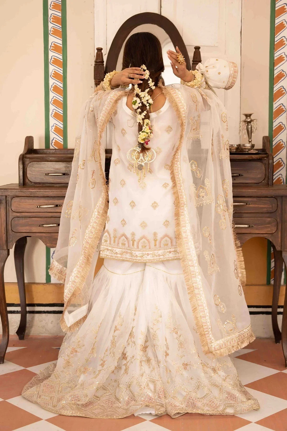 Elegant white embroidered bridal dress with gold detailing, floral hair accessories, and sheer dupatta for Pakistani weddings.
