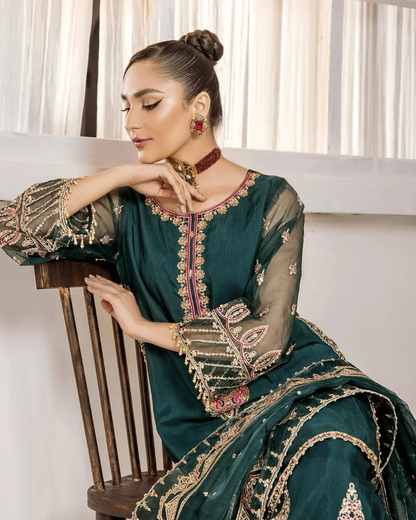 Woman in a teal embroidered traditional outfit sitting on a wooden chair.